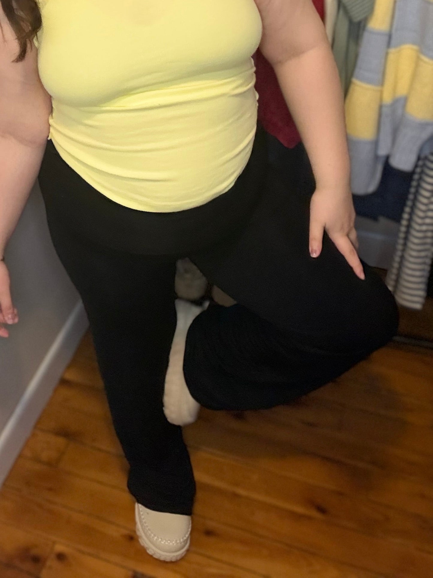Woman in a yellow top and black pants standing in front of a rack of clothes.