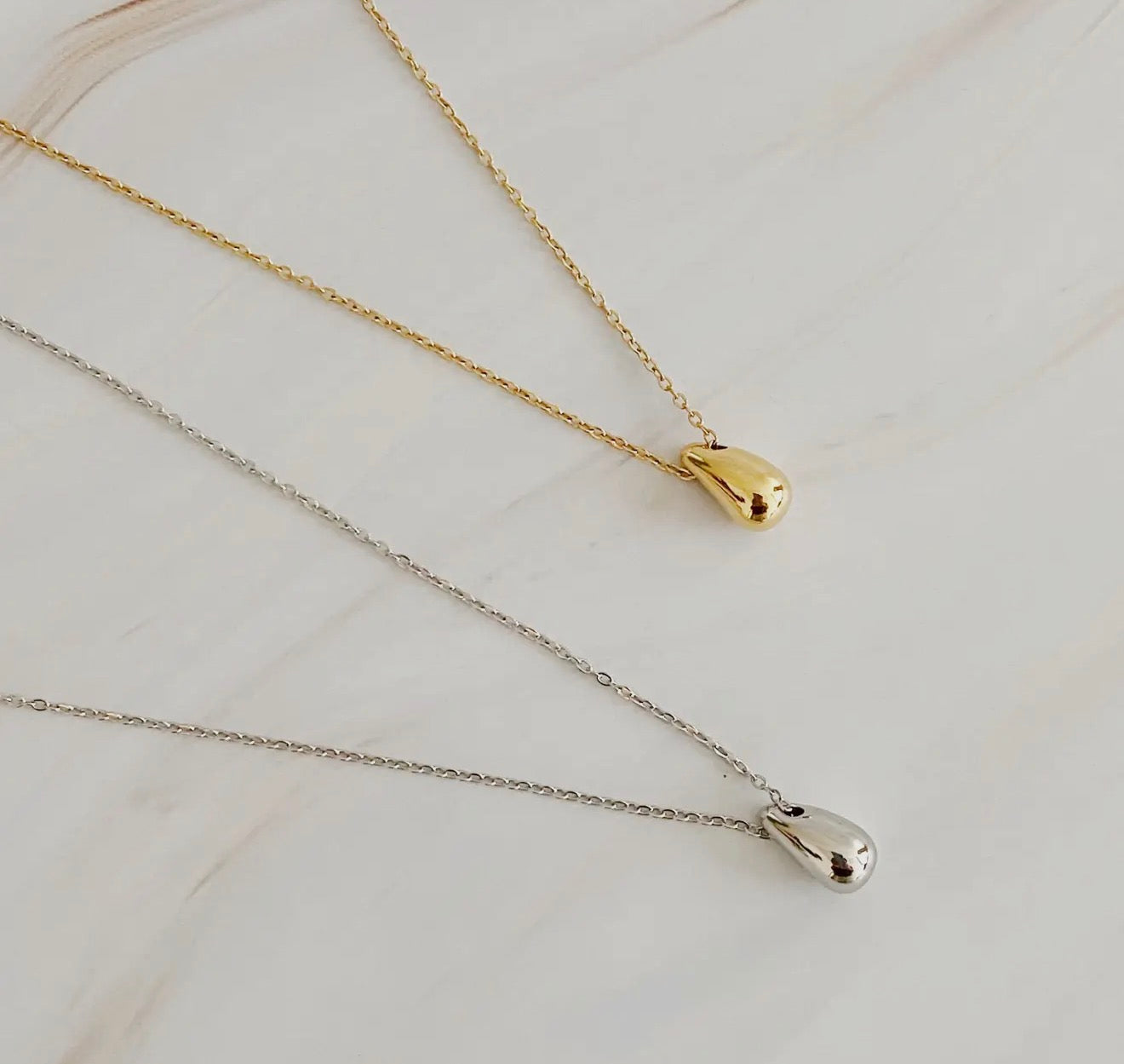 Two gold and silver necklaces with teardrop pendants on a light background