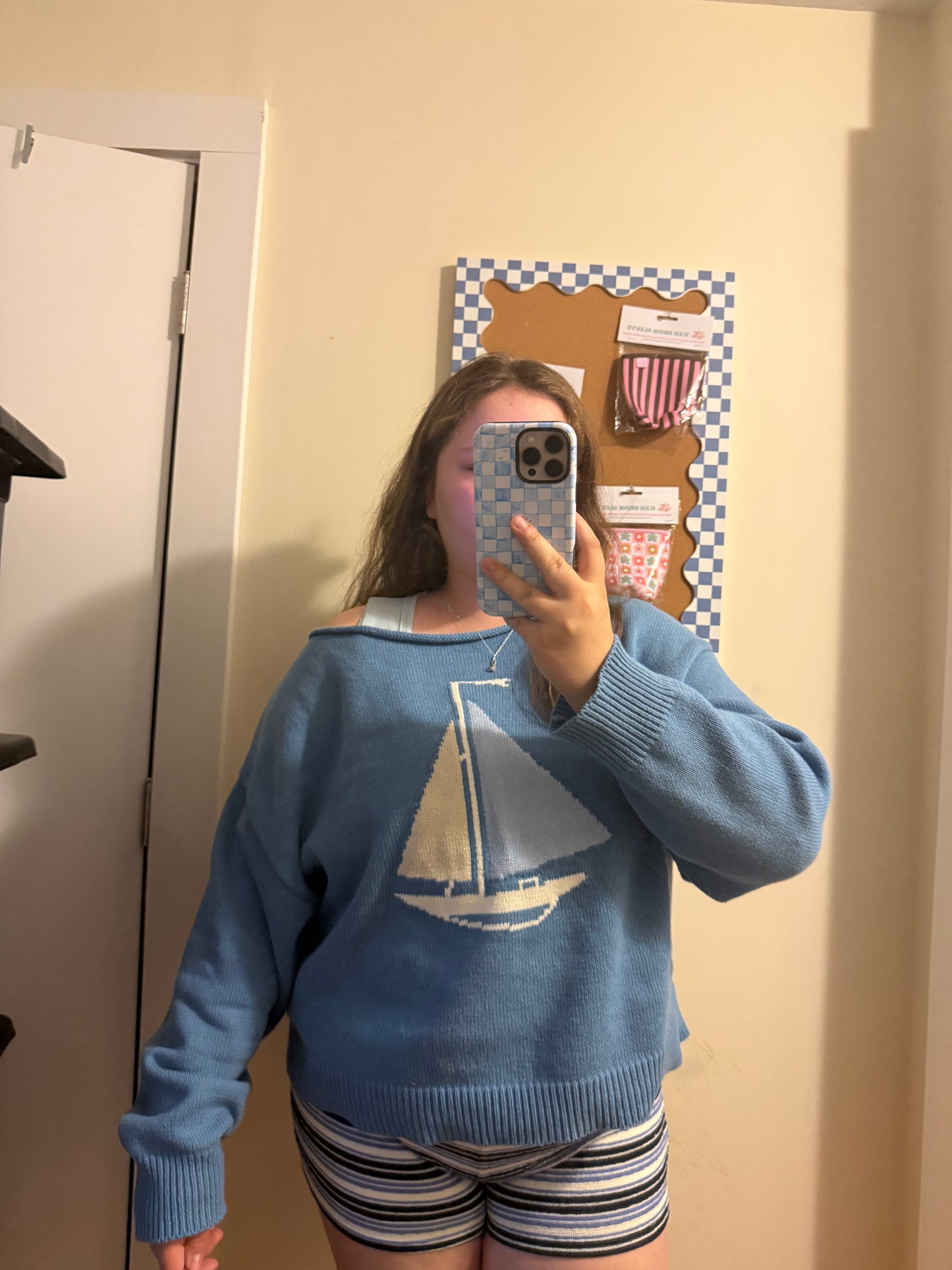 Person wearing a blue sweater with a sailboat design in a room.