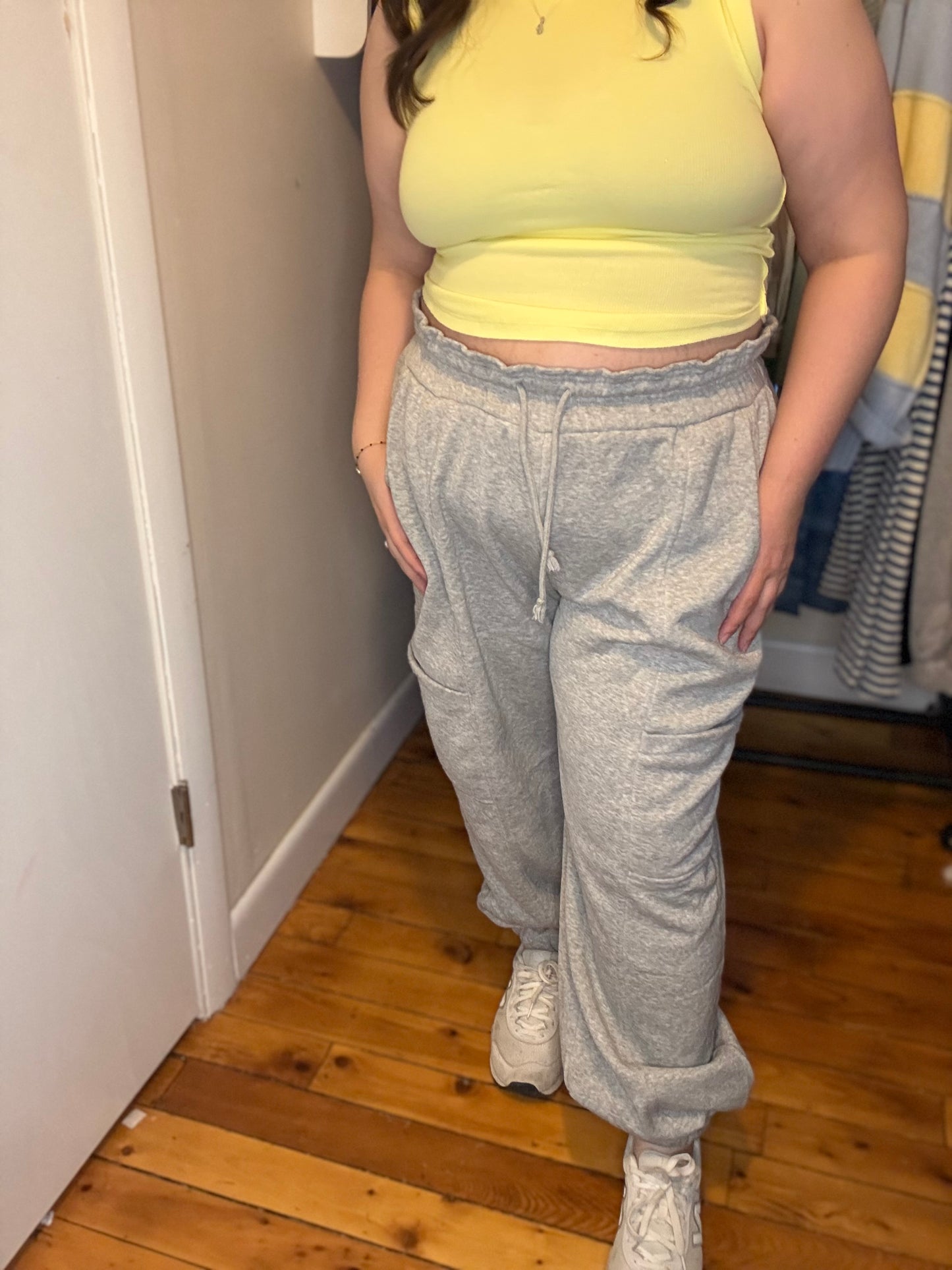 Person wearing a yellow tank top and gray sweatpants standing in a room with wooden flooring.