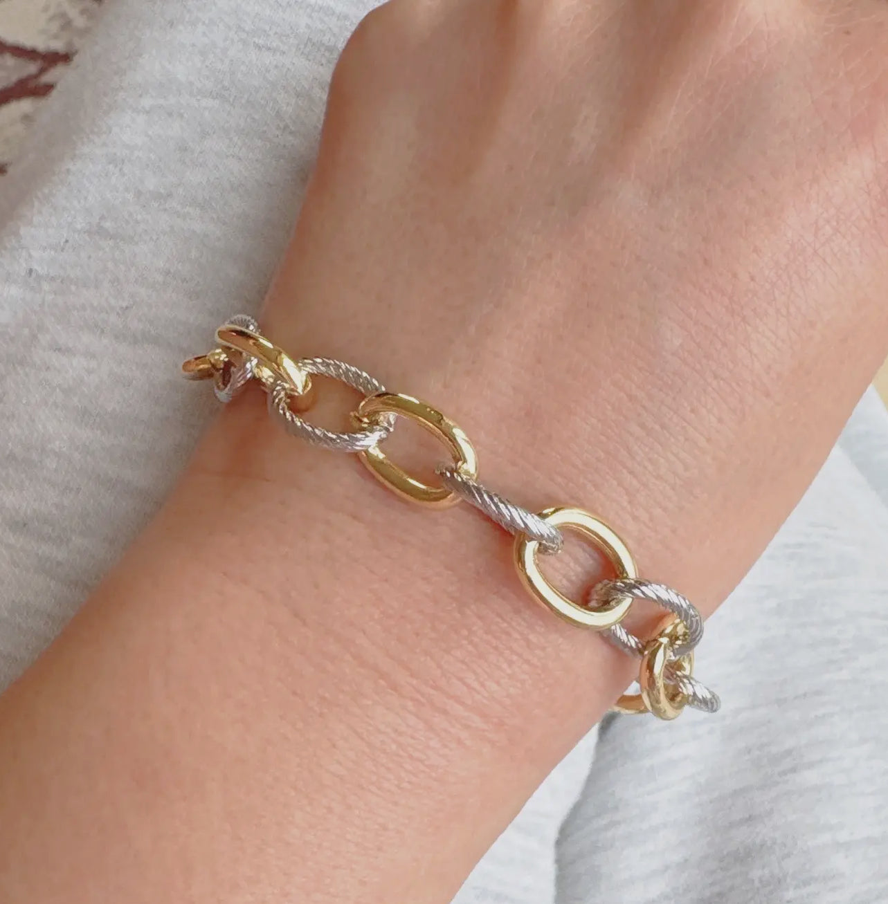 Gold and silver chain bracelet on a wrist against a neutral background