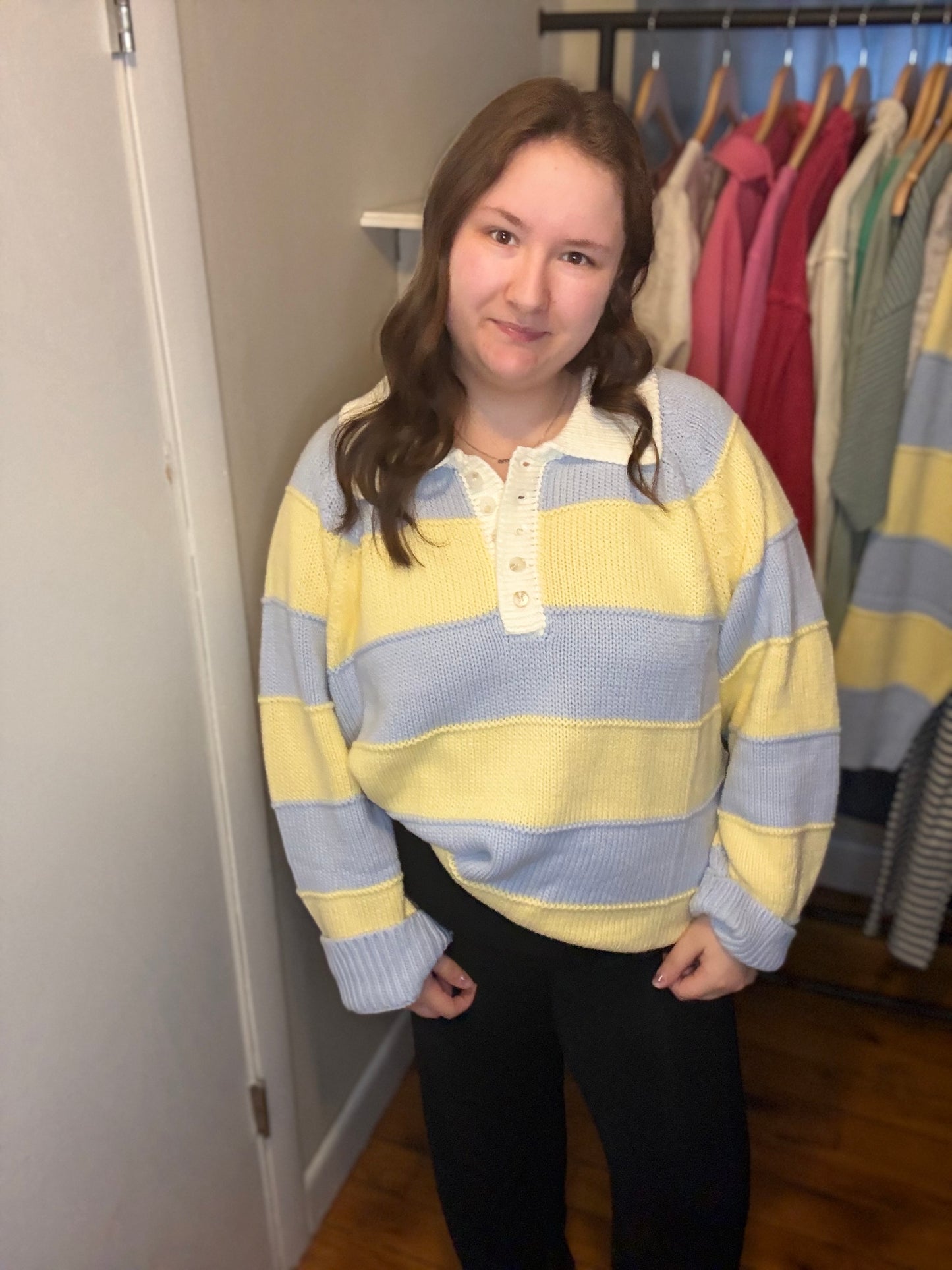 Person wearing a yellow and blue striped sweater in a room with clothes on hangers.