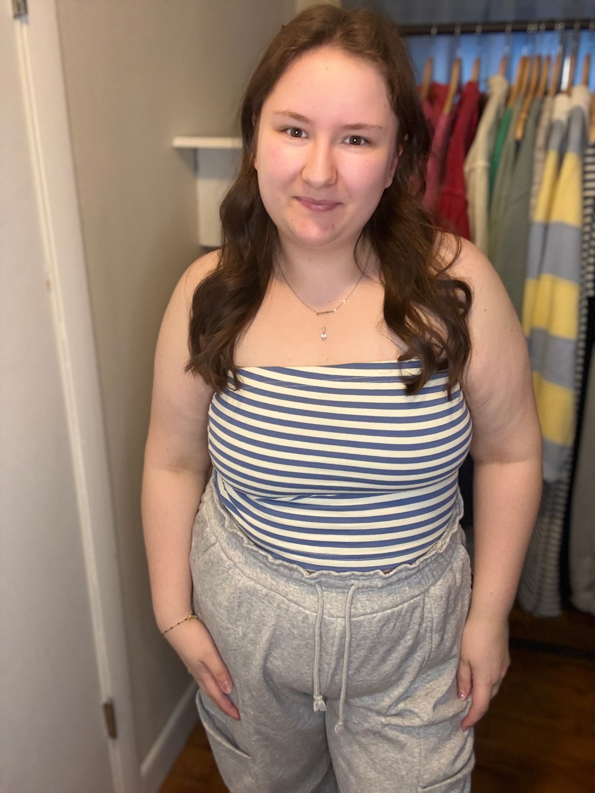 Woman wearing a striped tube top and gray sweatpants in a room with clothes on hangers.