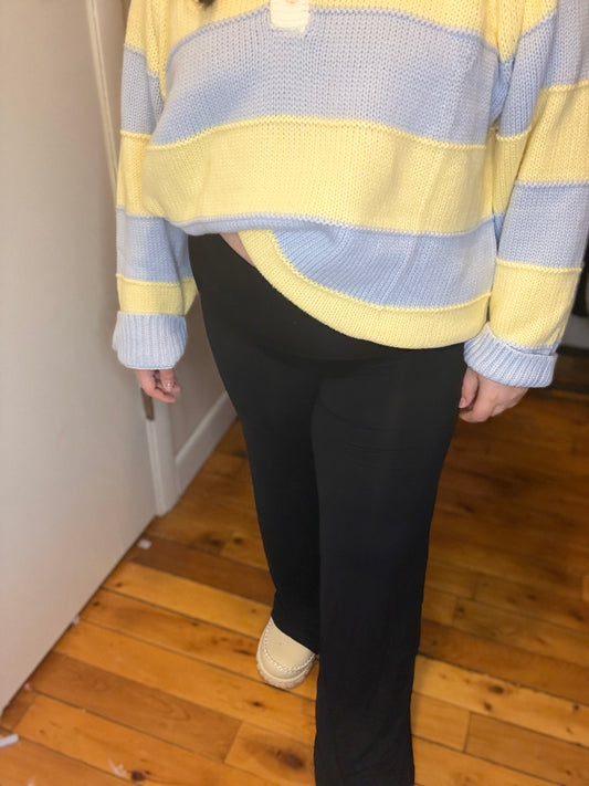 Person wearing a yellow and blue striped sweater and black leggings on a wooden floor.