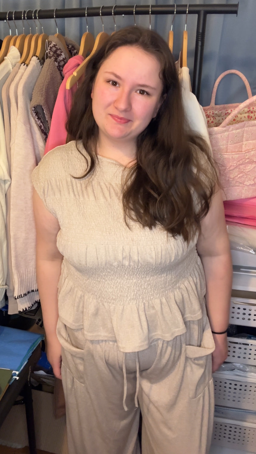 Woman wearing a beige outfit standing in front of a rack of clothes.
