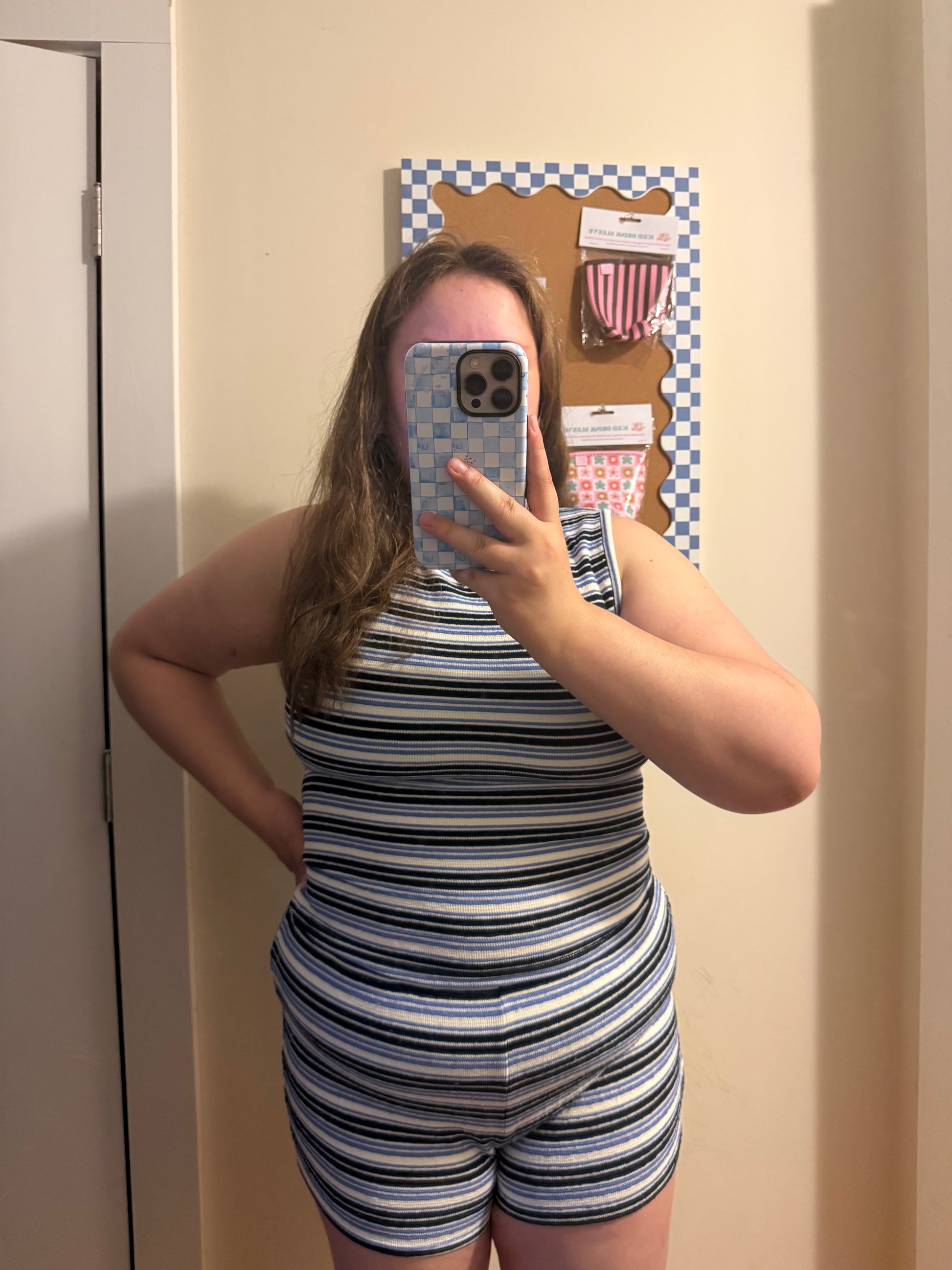 Person wearing a striped romper taking a mirror selfie.