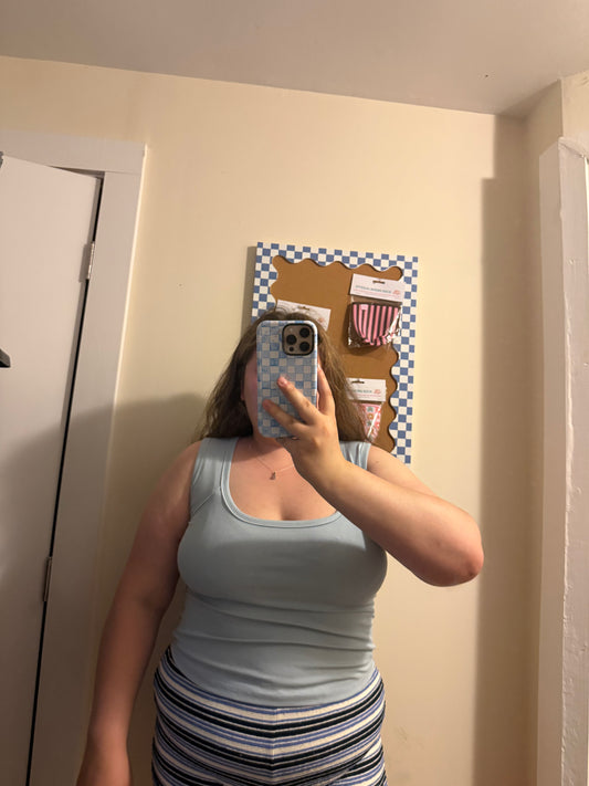 Person taking a mirror selfie wearing a light blue tank top and striped shorts