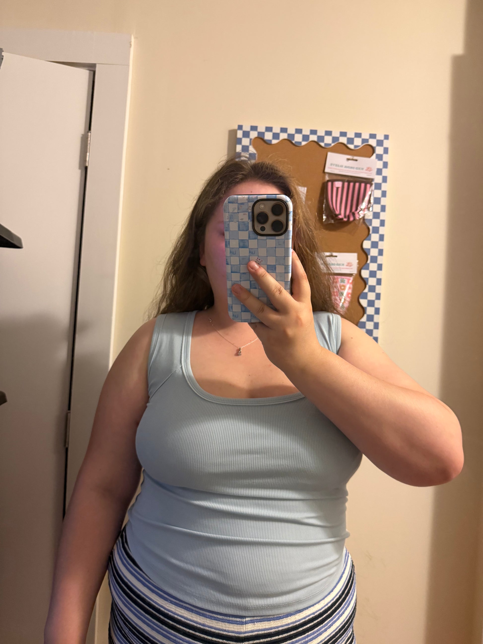 Person taking a mirror selfie wearing a light blue tank top and striped shorts