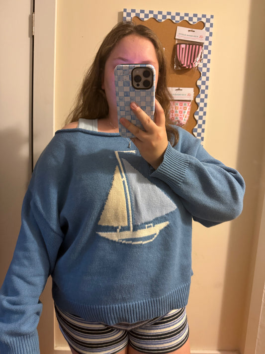 Person wearing a blue sweater with a sailboat design, taking a mirror selfie.
