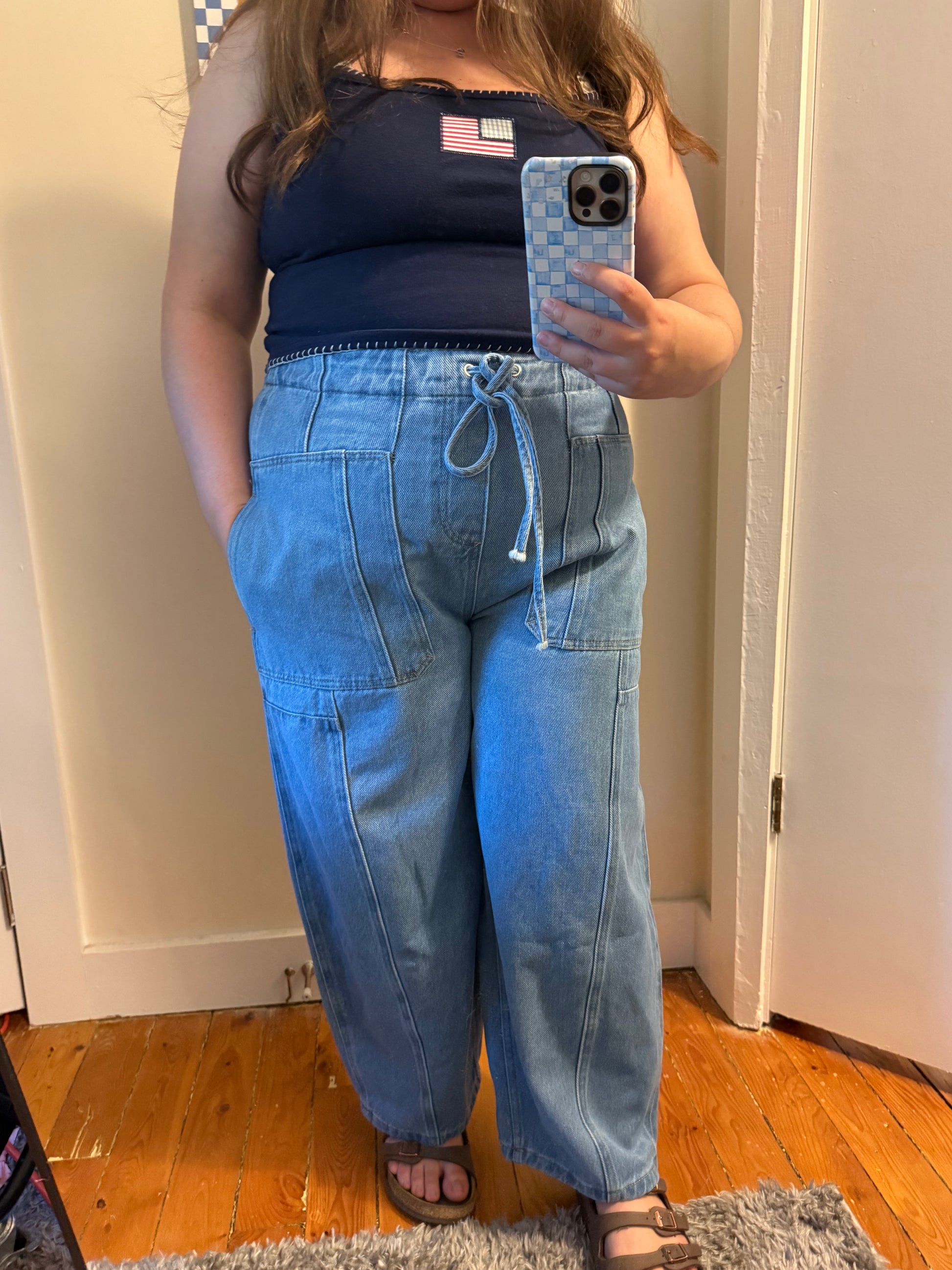 Person wearing a navy top and blue jeans taking a mirror selfie.