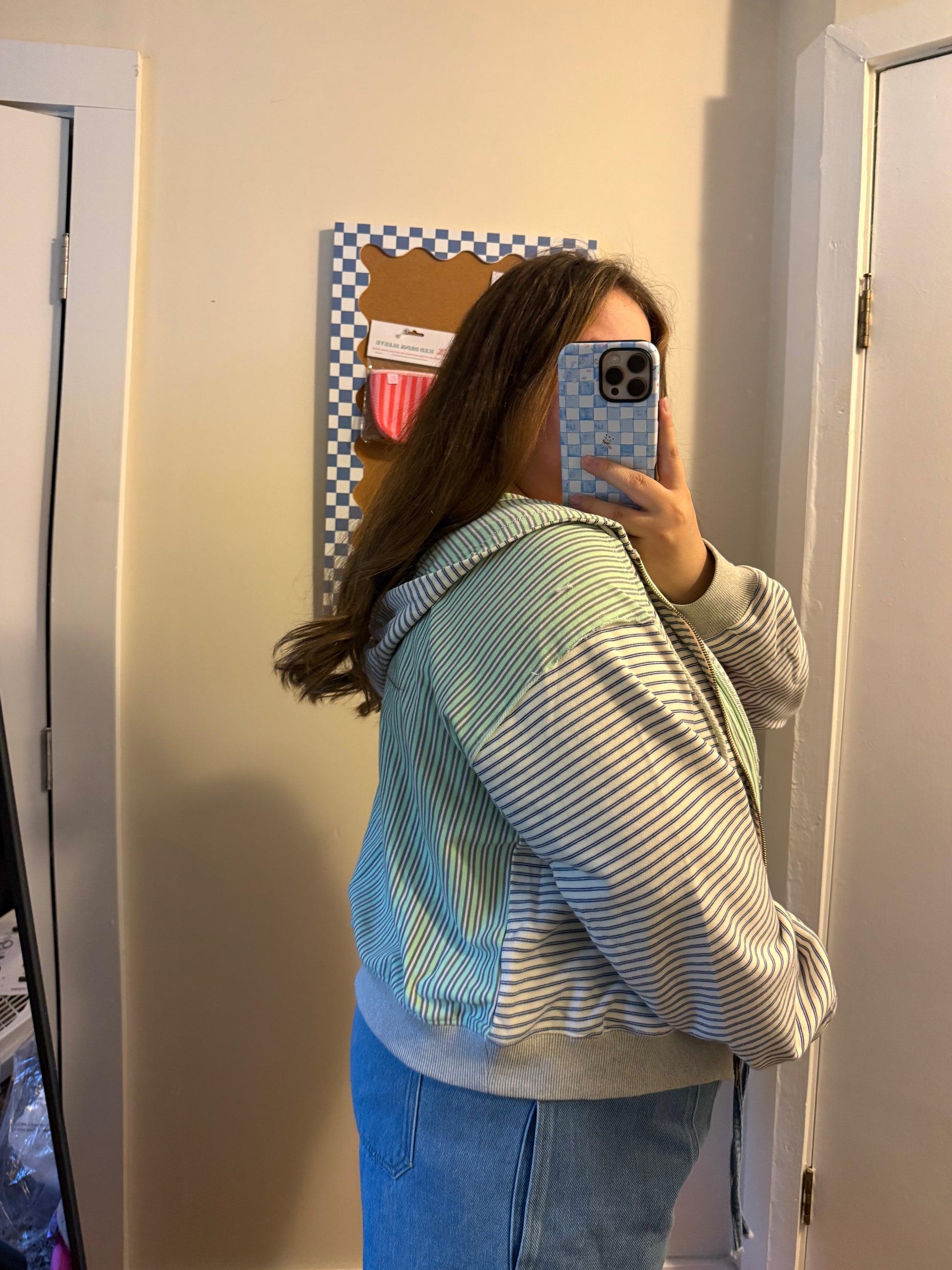 Person taking a mirror selfie wearing a striped jacket and blue jeans.