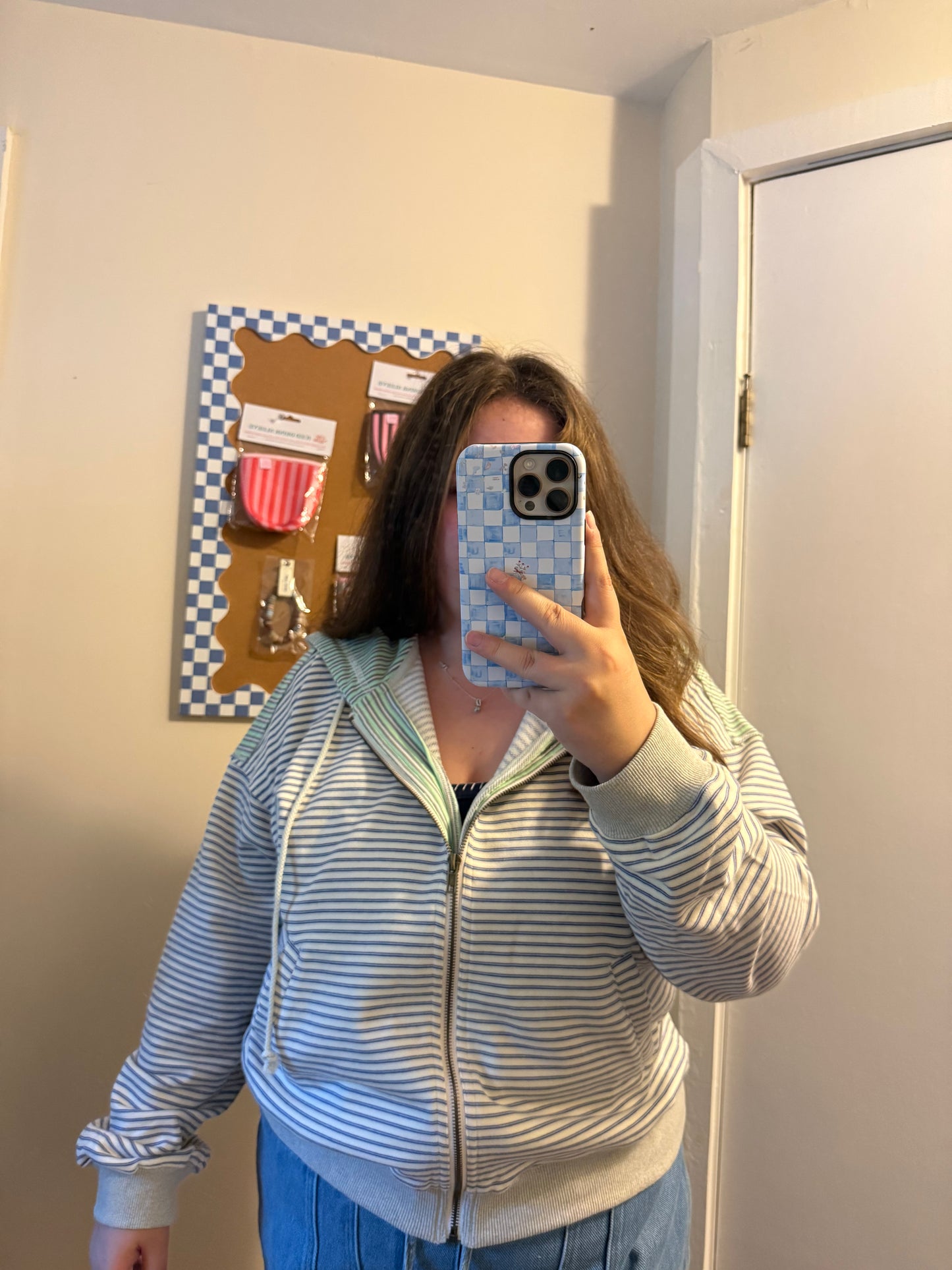 Person wearing a striped hoodie taking a mirror selfie in a room.