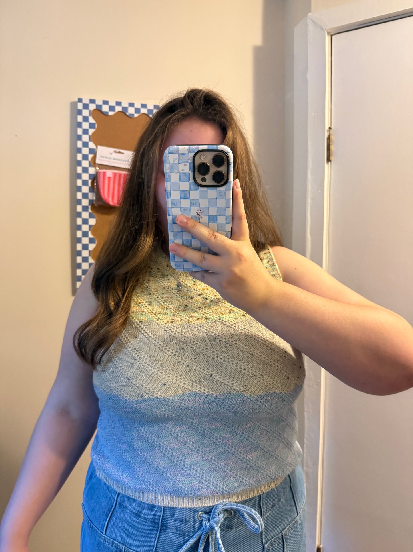 Person wearing a blue and white patterned sleeveless top taking a mirror selfie.