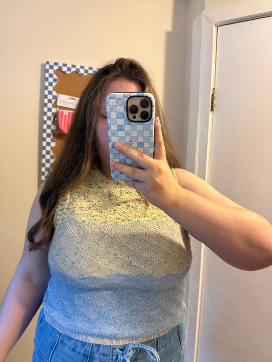Person wearing a blue and white patterned sleeveless top taking a mirror selfie.